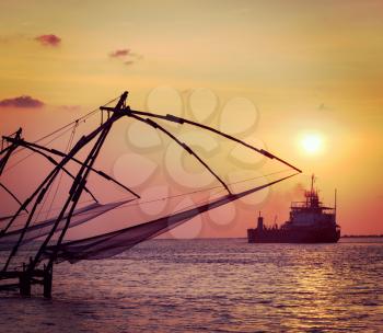 Vintage retro hipster style travel image of Kochi chinese fishnets on sunset and modern ship. Fort Kochin, Kochi, Kerala, India