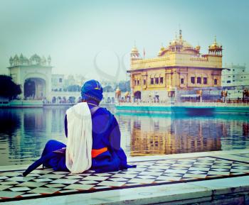 Vintage retro hipster style travel image of unidentifiable Seekh Nihang warrior meditating at Sikh temple Harmandir Sahib. Amritsar, India