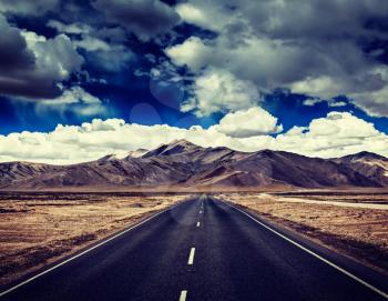 Vintage retro effect hipster style image of Travel forward concept background - road on plains in Himalayas with mountains and dramatic clouds. Manali-Leh road, Ladakh, Jammu and Kashmir, India
