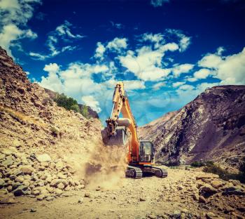 Vintage retro effect filtered hipster style travel image of Excavator doing road construction in Himalayas. Ladakh, Jammu and Kashmir, India