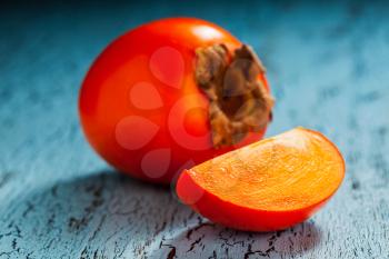 Fresh ripe persimmon with slice on a blue wooden background