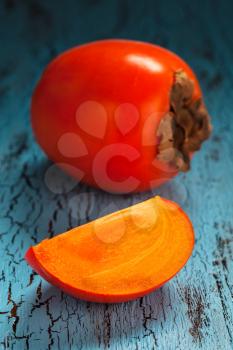 Fresh ripe persimmon with slice on a blue wooden background