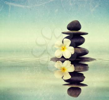 Vintage retro hipster style travel image of Zen spa concept background - Zen massage stones with frangipani plumeria flower in water reflection with grunge texture overlaid