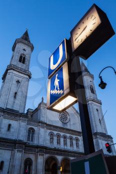 U-Bahn sign and St. Ludwig's Church (Ludwigskirche) in the evening.  Car Light Traces motion blur because of long exposure. Munich, Bavaria, Germany