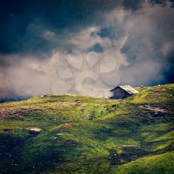 Serenity serene lonely scenery background concept - old house in hills in mountins on alpine meadow in clouds. VIntage style cross process, grain and texture added