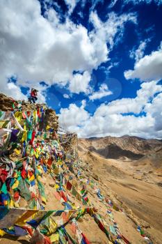 Travel photographer taking photos in Himalayas mountains on cliff with Buddhist prayer flags. Leh, Ladakh, Jammu and Kashmir, India