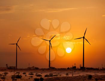 Green renewable energy concept - wind generator turbines sihouettes on sunset