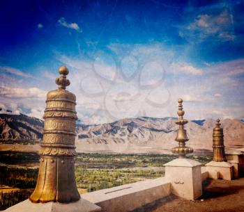 Vintage retro effect filtered hipster style travel image of Dhvaja victory banners, on the roof of Thiksey gompa monastery and view of Indus valley with grunge texture overlaid. Ladakh, India