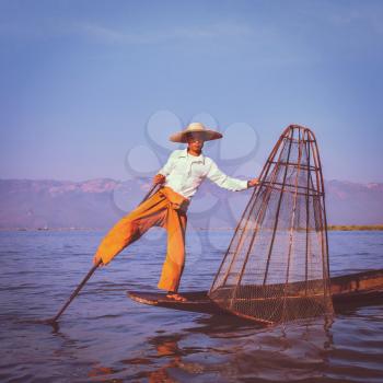 Vintage retro effect filtered hipster style image of Myanmar travel attraction. Traditional Burmese fisherman with fishing net at Inle lake famous for their distinctive one legged rowing style