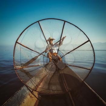 Myanmar travel attraction - Traditional Burmese fisherman with fishing net at Inle lake in Myanmar, view from boat. Vintage filtered retro effect hipster style image