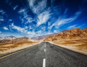 Travel forward concept background - road in mountains Himalayas with dramatic clouds on blue sky. Ladakh, Jammu and Kashmir, India