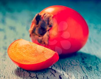 Vintage retro effect filtered hipster style image of fresh ripe persimmon with slice on a blue wooden background