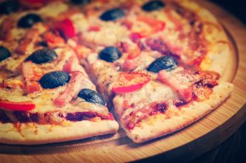 Vintage retro effect filtered hipster style image of sliced ham pizza with capsicum and olives on wooden board on table