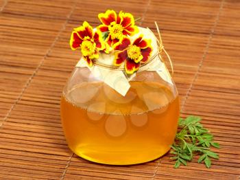 Honey jar and yellow flowers on a wooden surface.