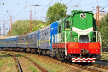 Green locomotive and blue passenger cars on the rails.