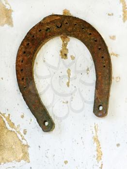 Old rusty lucky horseshoe on aged white clay wall background.