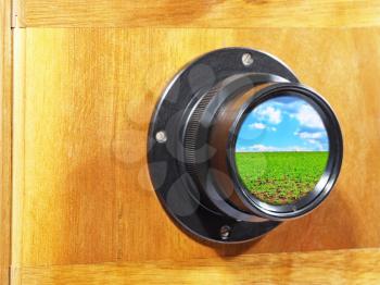 Old camera lens with blue sky and green grass inside.