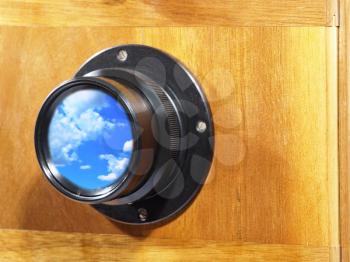 Old camera lens with blue sky and clouds inside.