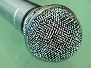 Silver metallic microphone taken closeup on blue background.