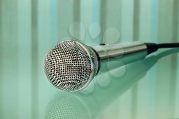 Silver metallic microphone on a striped transparent blue background.