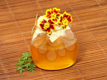 Honey jar and yellow flowers on a wooden surface.