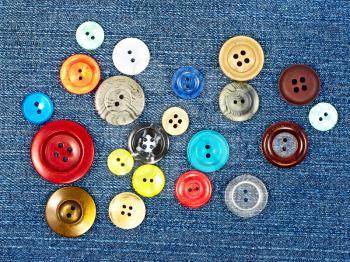Various sized multicoloured buttons on blue fabric as background.