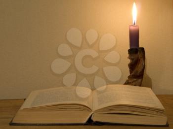 Old magic open book and  glowing candle on a wooden table.
