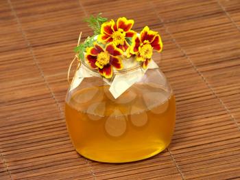Honey jar and yellow flower on a wooden surface.