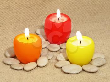 Three multicolored candles and small stones on a wool background.