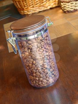Appetizing coffee beans in glass container on wooden table.
