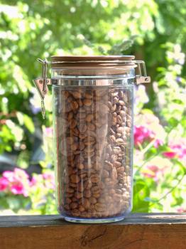 Coffee beans in glass container on green floral background..