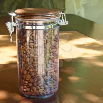 Coffee beans in transparent glass container on wooden table taken closeup.