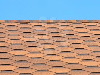 Bituminous tiles roof taken closeup against of blue sky.