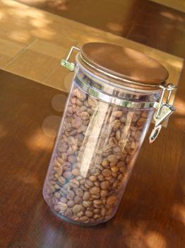 Coffee beans in glass container on wooden table taken closeup.