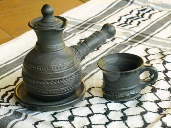 Ceramic coffeepot and cup on a white keffiyah scarf taken closeup.
