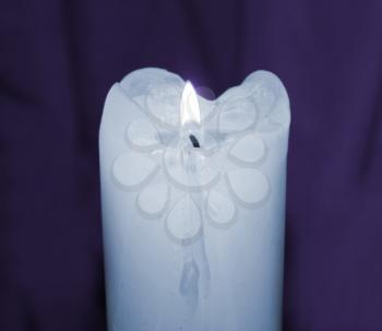 Glowing mourning candle in darkness taken closeup on purple.