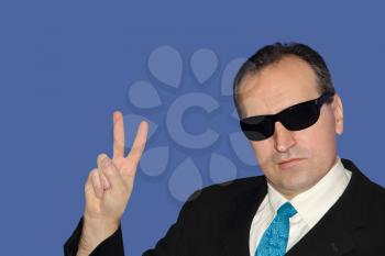 Man in black showing the victory sign on blue background.