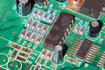 Green electronic microcircuit with microchips and capacitors taken closeup.