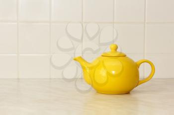Yellow ceramic teapot on white kitchen table and ceramic tile background.