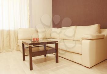 Modern beige corner leather sofa and coffee table in room.