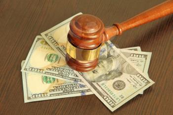 Judge gavel and dollar banknotes on wooden table taken closeup.