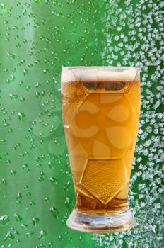 Froth beer glass taken closeup on ice crystals and drips green background.