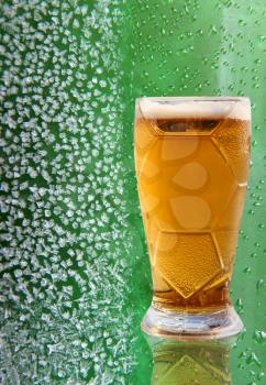 Fresh beer glass with reflection on ice crystals and drips green background.