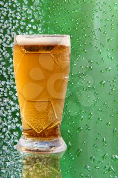 Froth beer glass with reflection on ice crystals and drips green background.