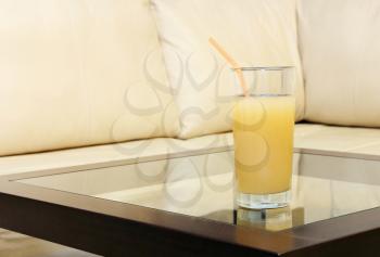 Glass juice and cocktail straw on transparent table against of the white leather sofa.