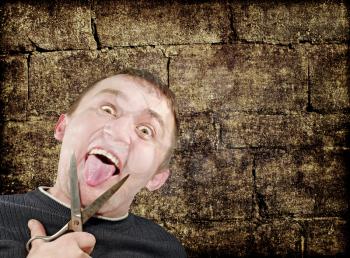 Mad man with scissors cuts off itself tongue on grunge brick wall background.