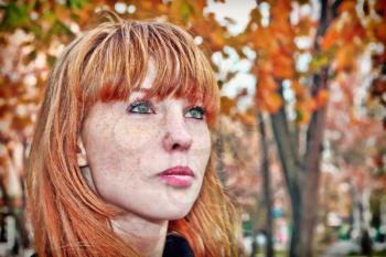 Pretty red hair girl face with freckles against autumn foliage. Digitally altered image.