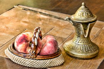 Retro arabian style brass coffee pot and ceramic vase with peaches on a table.Soft toned image.