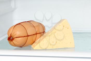 Fresh appetizing sausage and cheese piece on refrigerator shelf taken closeup.