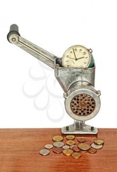 Money concept.Alarm clock in manual meat grinder and coins on wooden table.